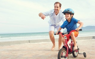 Father and son learning to ride a bicycle at the beach having fun together